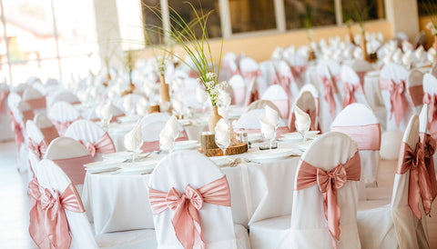 Eleganter Empfangsraum mit weißen Stuhlhussen, puderrosa Schleifen und Hochzeitstafel